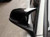 A black side mirror reflects surroundings, attached to a white vehicle, positioned on a paved street.