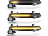 Three elongated car side mirror indicators display amber lights. Each indicator has a translucent cover and mounting brackets, set against a plain white background.