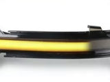 A sleek, elongated car side mirror indicator with a glowing yellow strip is mounted on a black housing, set against a plain white background.