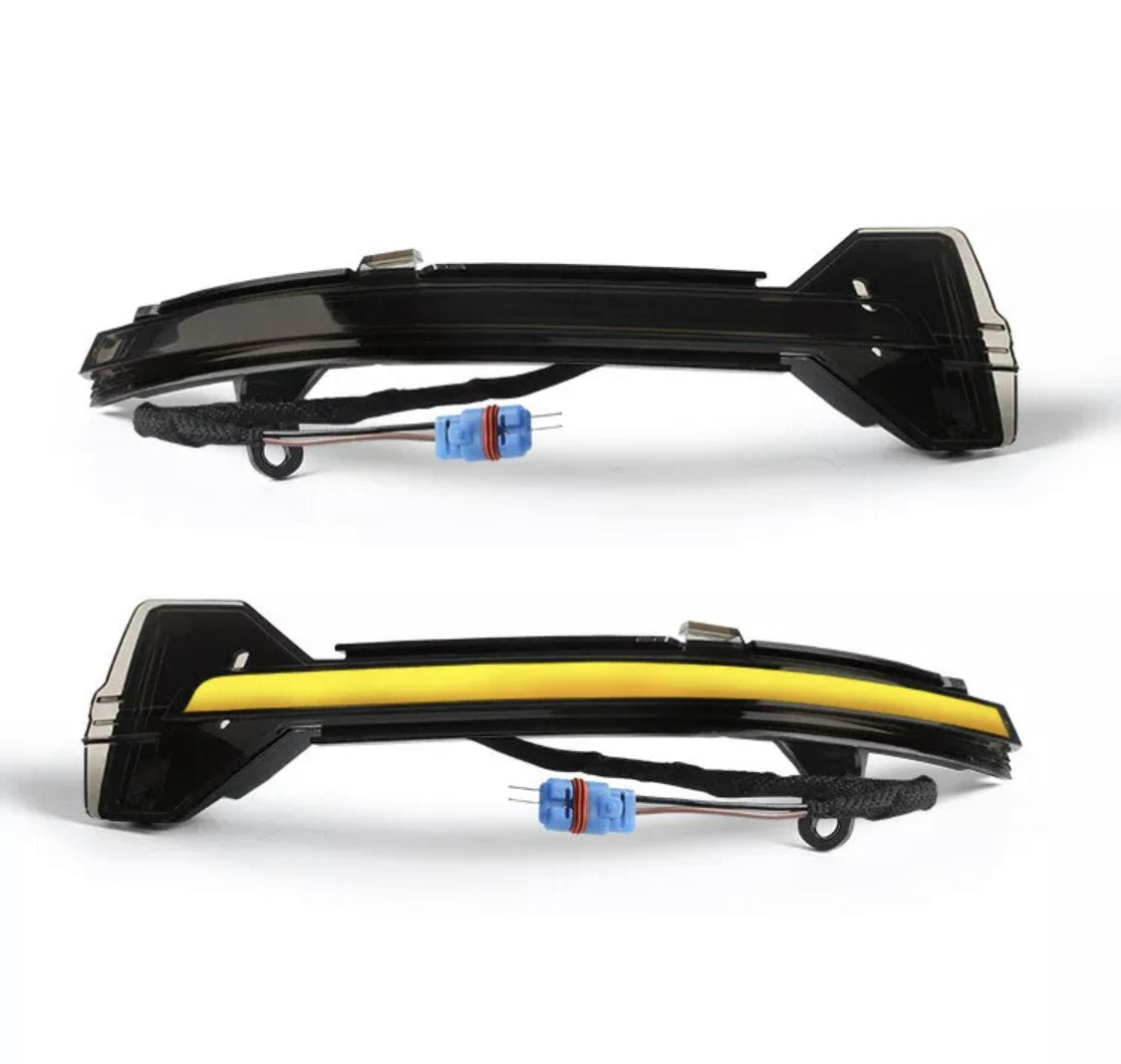 Car side mirror indicators with wiring exposed, shown from a side view. The top indicator is inactive; the bottom one is illuminated with a yellow light, both on a white background.