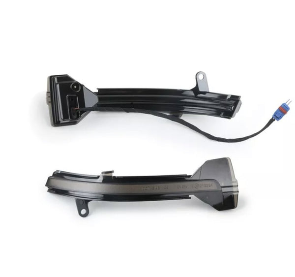 Two black, curved plastic car mirror indicators, one with an attached cable and connector, lie on a white background. They are designed to fit onto the side mirrors of a vehicle.