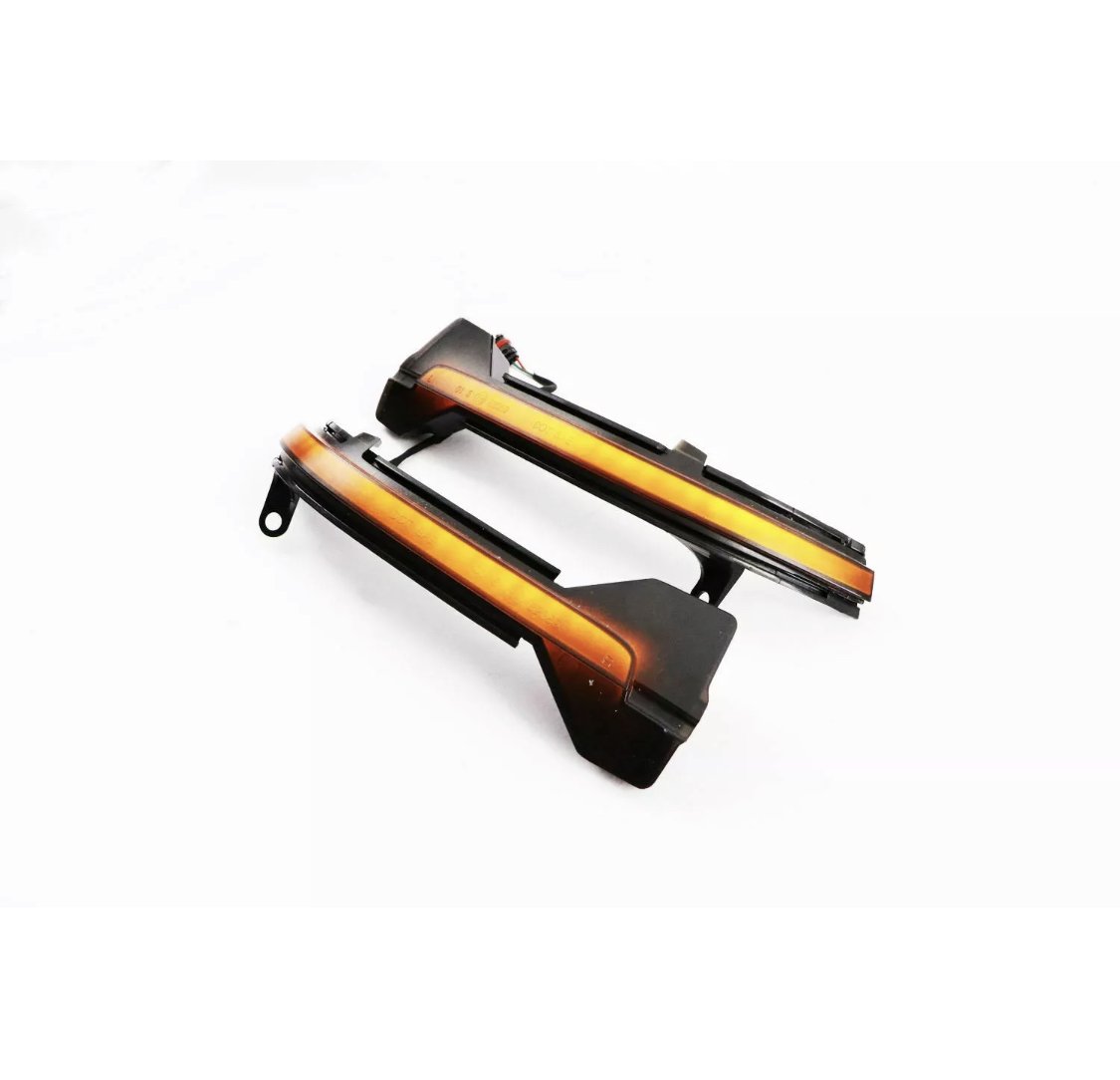 Two black car side mirrors with integrated amber LED indicator strips, placed on a white background. They exhibit sleek, angular design elements typical of modern automotive components.