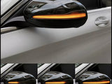 A car's side mirror with an integrated amber light blinking sequentially, mounted on a white vehicle, shown in multiple frames captured from the side.
