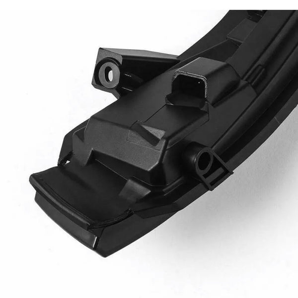 A black, angular, plastic automotive component with a rectangular connector port sits on a smooth, white background, featuring mounting points and a sleek, modern design.