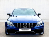 A blue luxury car is parked on a paved surface, facing forward. Its front grille features a prominent emblem. The background is a plain, light-colored wall. Text reads: 