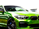 A vibrant green sports car is parked on a paved surface. It features sleek black wheels and distinctive headlights, set against a white building in the background.