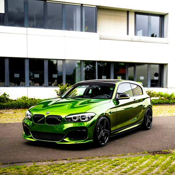 A vibrant green car parked on a paved surface, in front of a modern building with large windows and greenery along the base.
