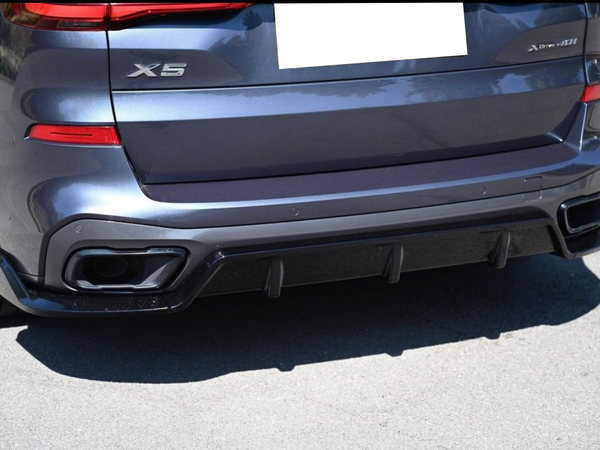 The rear of a dark-colored SUV features "X5" and "xDrive40i" badges. It is parked on a sunny street with visible dual exhaust outlets and red taillights.