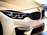 A gold BMW car with sleek front headlights and grille, parked on a snowy ground, showcasing its elegant design and smooth finish.