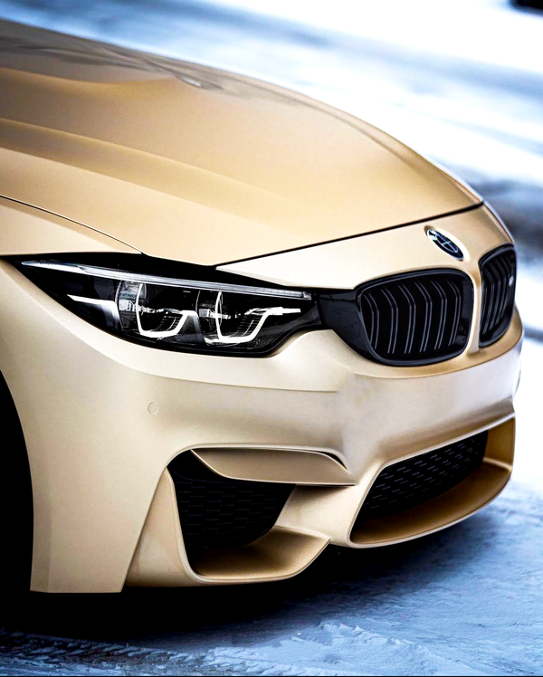 A gold BMW car with sleek front headlights and grille, parked on a snowy ground, showcasing its elegant design and smooth finish.