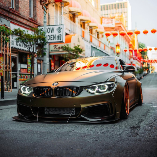 A sleek, customized BMW with lowered suspension parked on a street in Chinatown, surrounded by traditional architecture and red lanterns, creating a vibrant, urban setting.