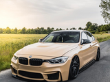 A sleek, beige BMW car parked on a rural road beside green fields during sunset, with trees visible in the background, under a partly cloudy sky.