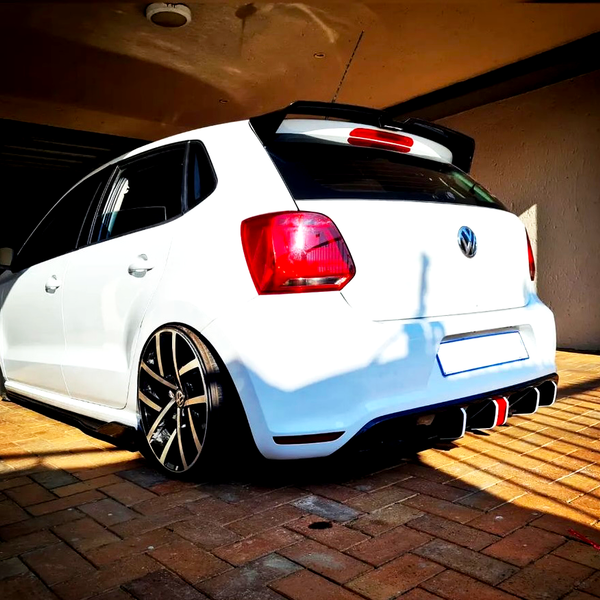 A white car parked on a brick driveway under a shaded carport. The car features large, black alloy wheels and a distinctive rear bumper. Shadows create a contrasting pattern on the ground.