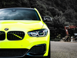 A bright yellow BMW car stands parked on a road, its sleek design contrasting with a forested hillside in the background. The environment appears rural with scattered machinery visible.