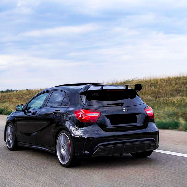 A black car is driving on an open highway, flanked by grassy fields, under a cloudy sky.
