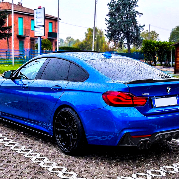 Blue BMW car parked, covered in raindrops, in a brick-paved lot with a wooden shed and trees in the background. Text includes “BMW,” "X Drive," and "420i".