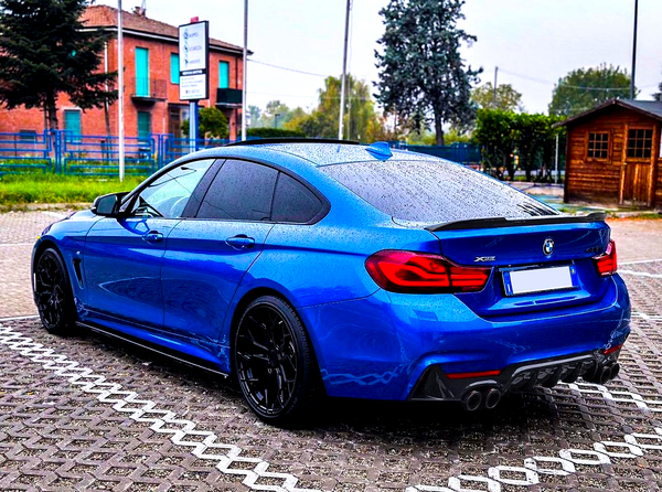 Blue BMW car parked, covered in raindrops, in a brick-paved lot with a wooden shed and trees in the background. Text includes “BMW,” "X Drive," and "420i".