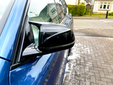 A blue car with a black side mirror is parked on a residential street, surrounded by houses and a hedge. Soapy residue is visible on the paved driveway.