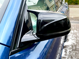 A black side mirror is attached to a blue car, parked on a wet, sudsy driveway beneath residential houses.