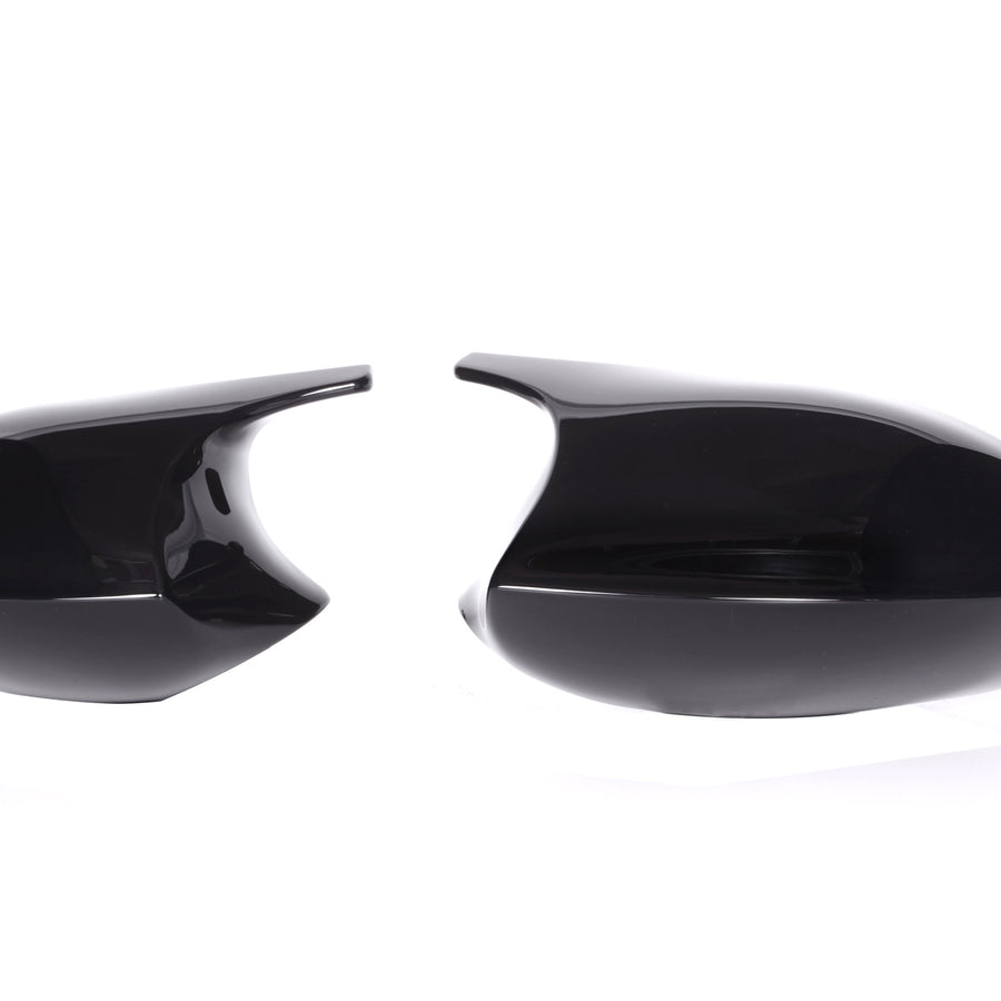 Two glossy black side mirror covers are placed against a white background, one on the left and one on the right, separated by space.