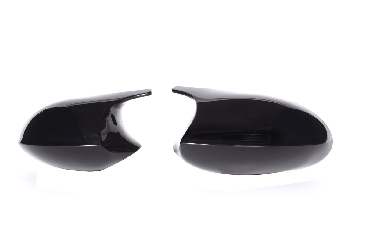 Two glossy black side mirror covers are placed against a white background, one on the left and one on the right, separated by space.