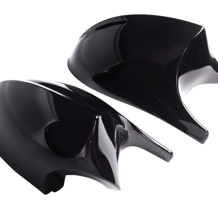 Two shiny black car mirror covers rest side by side against a plain white background, reflecting light on their smooth surfaces.
