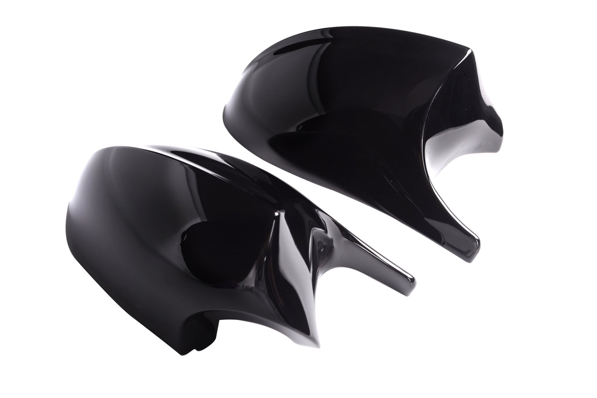 Two sleek, glossy black car mirror covers rest on a white background, reflecting light. The aerodynamic design suggests a modern vehicle accessory, with each piece symmetrical and curved.