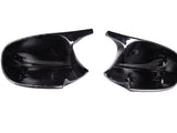 Two black plastic car mirror covers lie side by side, displaying attachment clips inside. They rest on a plain white background, illustrating their smooth, reflective surfaces and curved shapes.