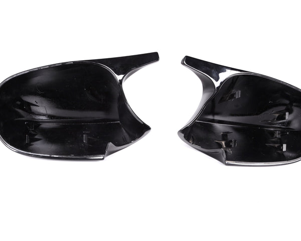 Two black plastic car mirror covers lie side by side, displaying attachment clips inside. They rest on a plain white background, illustrating their smooth, reflective surfaces and curved shapes.