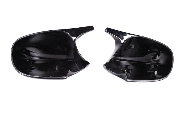 Two black plastic car mirror covers lie side by side, displaying attachment clips inside. They rest on a plain white background, illustrating their smooth, reflective surfaces and curved shapes.
