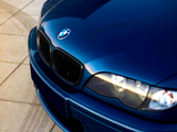 A blue BMW car is parked on a tiled surface, with the focus on its front bumper and headlights, reflecting natural light.