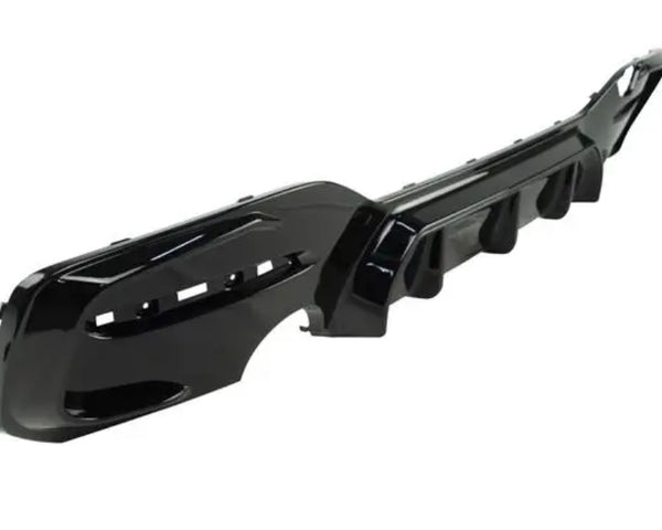 A glossy black car bumper with vent openings lies on a plain white background, displaying an angular, aerodynamic design.