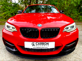 A red BMW car is parked on a concrete surface, front view, with trees in the background. The license plate reads, 