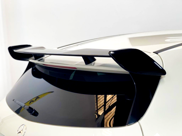 A sleek black car spoiler is mounted on the rear of a white vehicle, above a tinted back window with a visible wiper, in a well-lit indoor setting.