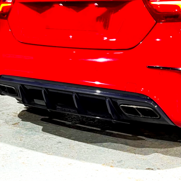 A red car with sleek taillights is parked, showcasing its rear bumper and dual exhaust outlets, on a concrete surface adjacent to a black and white wall.
