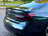 A sleek, dark-colored car is parked on a cobblestone path, surrounded by greenery. The focus is on its rear, with shiny tail lights and a visible BMW logo.