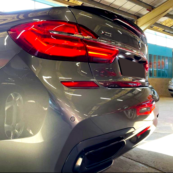 A gray BMW X5 car, parked indoors with illuminated brake lights, reflects its surroundings. Nearby, a silver Mercedes-Benz displays the license plate "FP62 GHU" in the bright-lit garage.