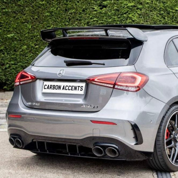 A silver Mercedes-Benz A250 has a prominent rear spoiler and dual exhausts, parked on a driveway with a hedge backdrop. The license plate reads "CARBON ACCENTS."