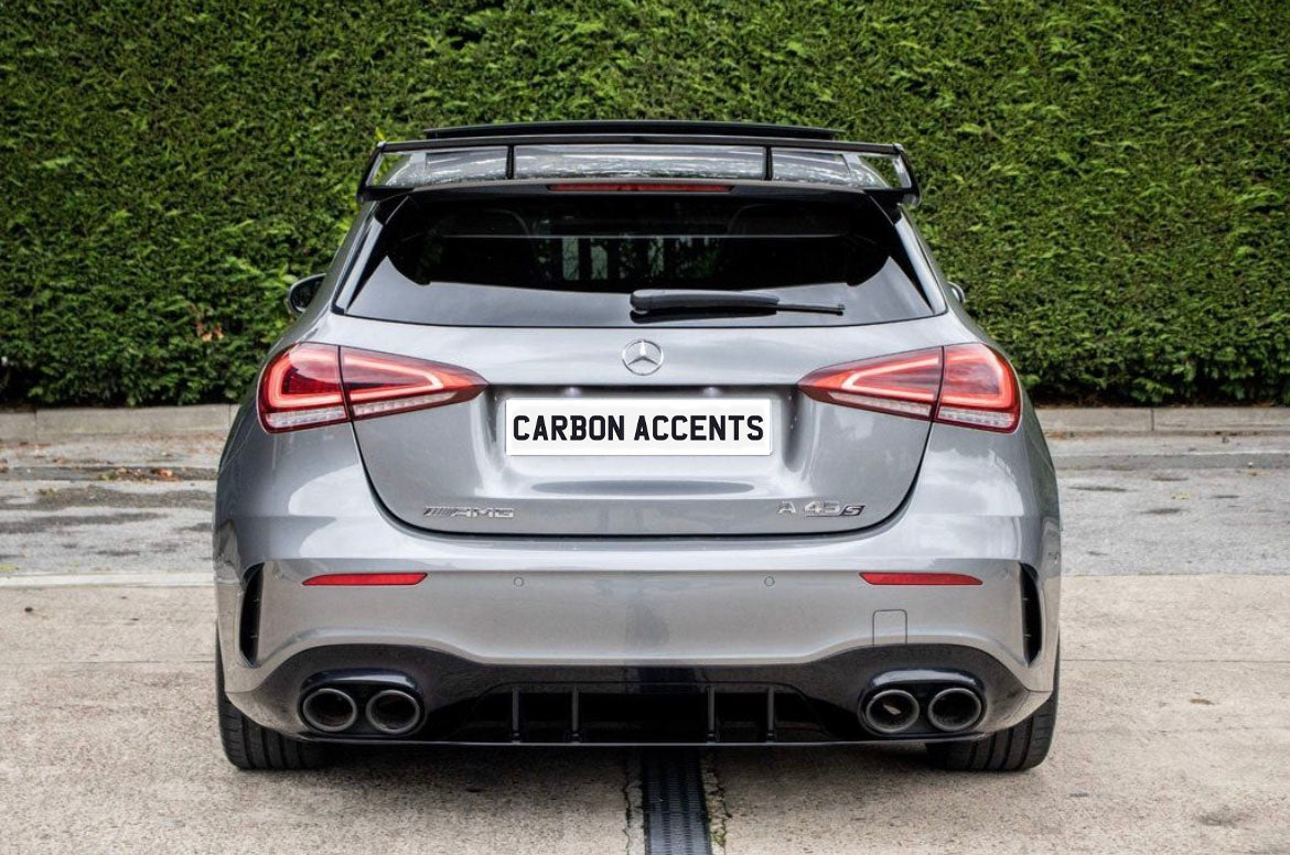 A silver Mercedes-Benz hatchback (AMG A 45 S) is parked on concrete. The license plate reads "CARBON ACCENTS," with dense greenery in the background.