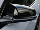A sleek, shiny side mirror on a car reflects its surroundings in close-up view, showcasing its aerodynamic design, with a blurred urban backdrop in the distance.
