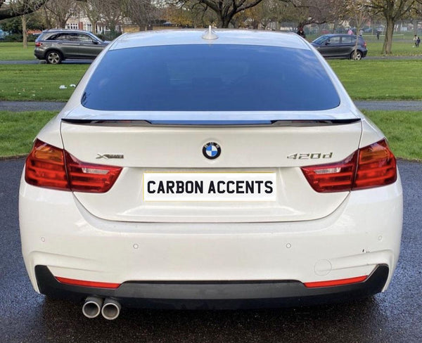 A white BMW 420d is parked on a paved path, with "CARBON ACCENTS" displayed on its license plate, surrounded by green lawns and other parked cars in a park setting.