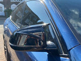 Car mirror reflects surrounding houses; blue vehicle parked on brick driveway under clear sky.