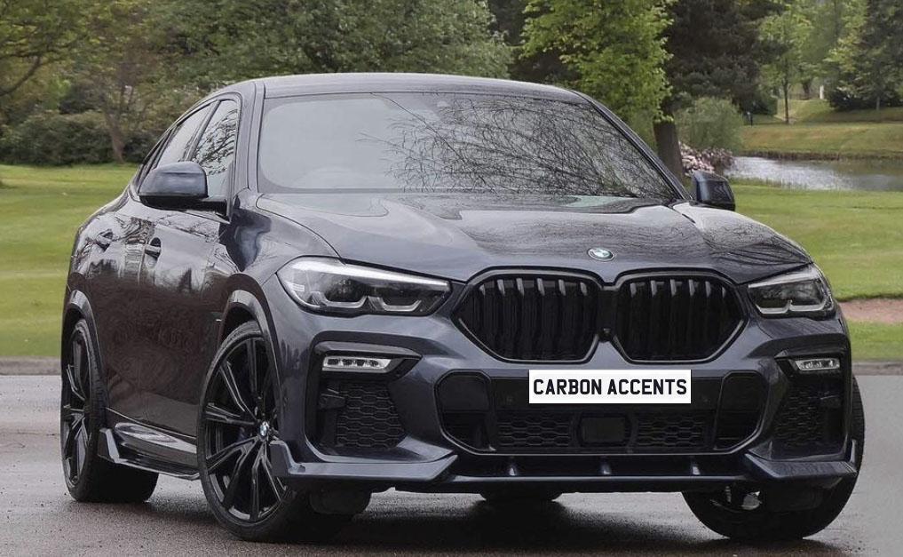 A sleek dark-colored BMW SUV is parked on a paved surface, surrounded by lush greenery and a pond. The license plate reads "CARBON ACCENTS."