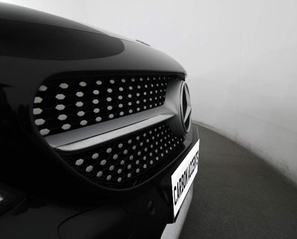 A car's front grille features a prominent logo with a pattern of hexagonal elements. It is parked in a well-lit garage. The visible text reads "CARBON ACCENTS."